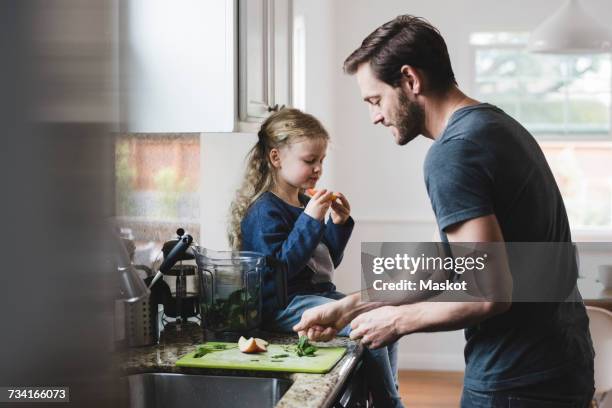 side view of father cooking food while daughter having apple in kitchen - menta familia de plantas fotografías e imágenes de stock
