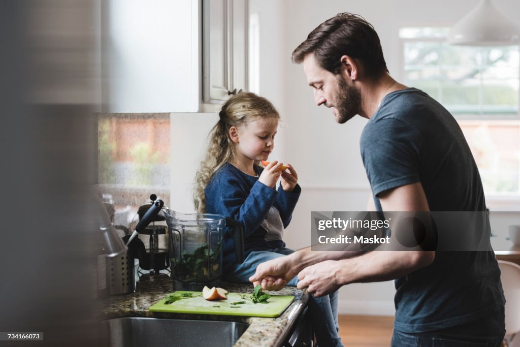 Side view of father cooking food while daughter having apple in kitchen