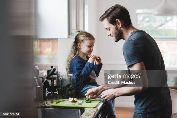 side view of father cooking food while daughter having apple in kitchen - cookery stock pictures, royalty-free photos & images