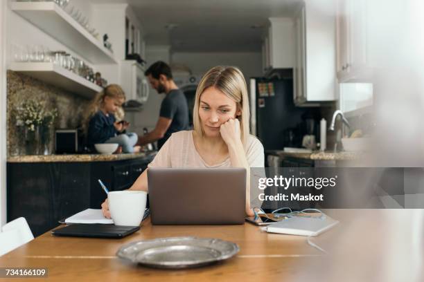 mid adult woman using laptop at table with family in kitchen at home - venice couple fotografías e imágenes de stock