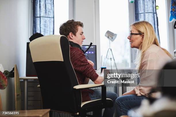 Mother talking to son sitting by computer at home