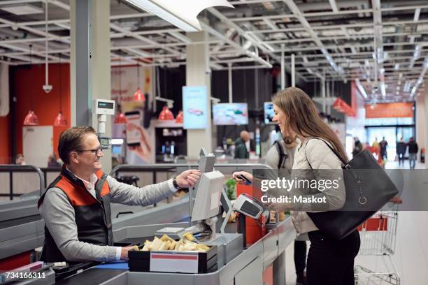 mature cashier talking to woman while paying at checkout counter in supermarket - checkers - fotografias e filmes do acervo