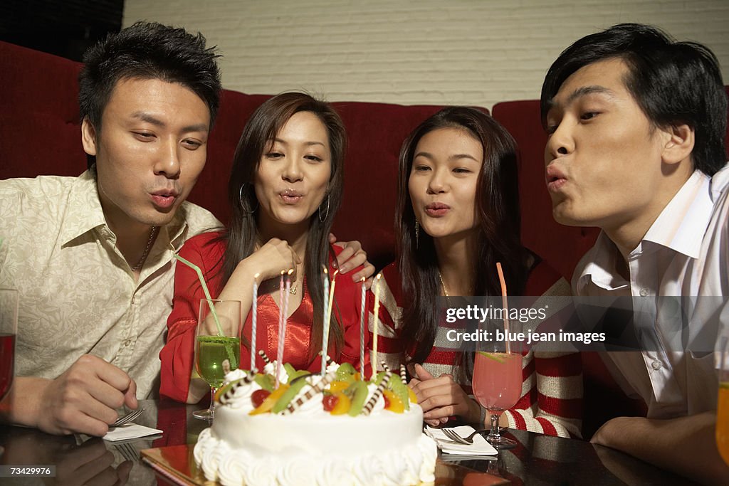 Two young men and two young women blowing the candles of a birthday cake.