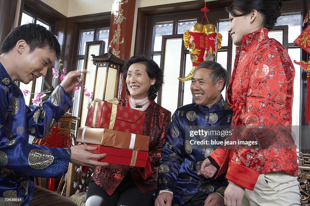 A mature adult son and his wife present presents to his parents as they visit their traditional courtyard home during Chinese New Year.