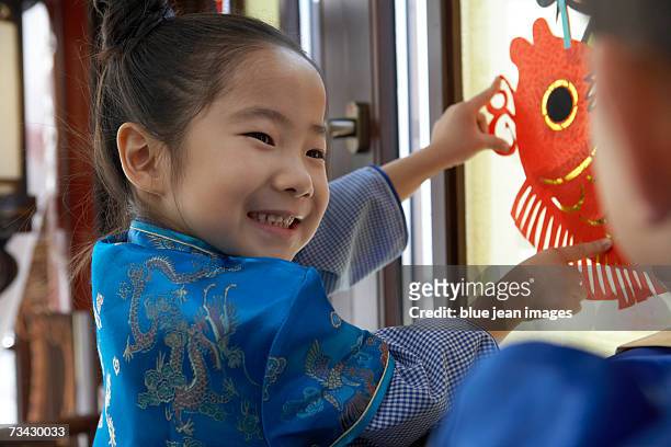 a young boy and young girl dressed in traditional attire fix a colorful paper cutout to the window during a visit to their grandparents' courtyard home over chinese new year. - fixpunkt stock-fotos und bilder