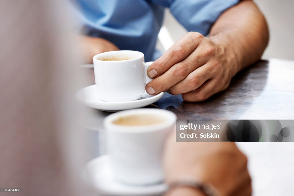 Two people drinking espresso at outdoor cafe, close-up of hands