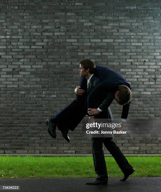 business man carrying colleague on shoulder, side view - person auf den schultern tragen stock-fotos und bilder