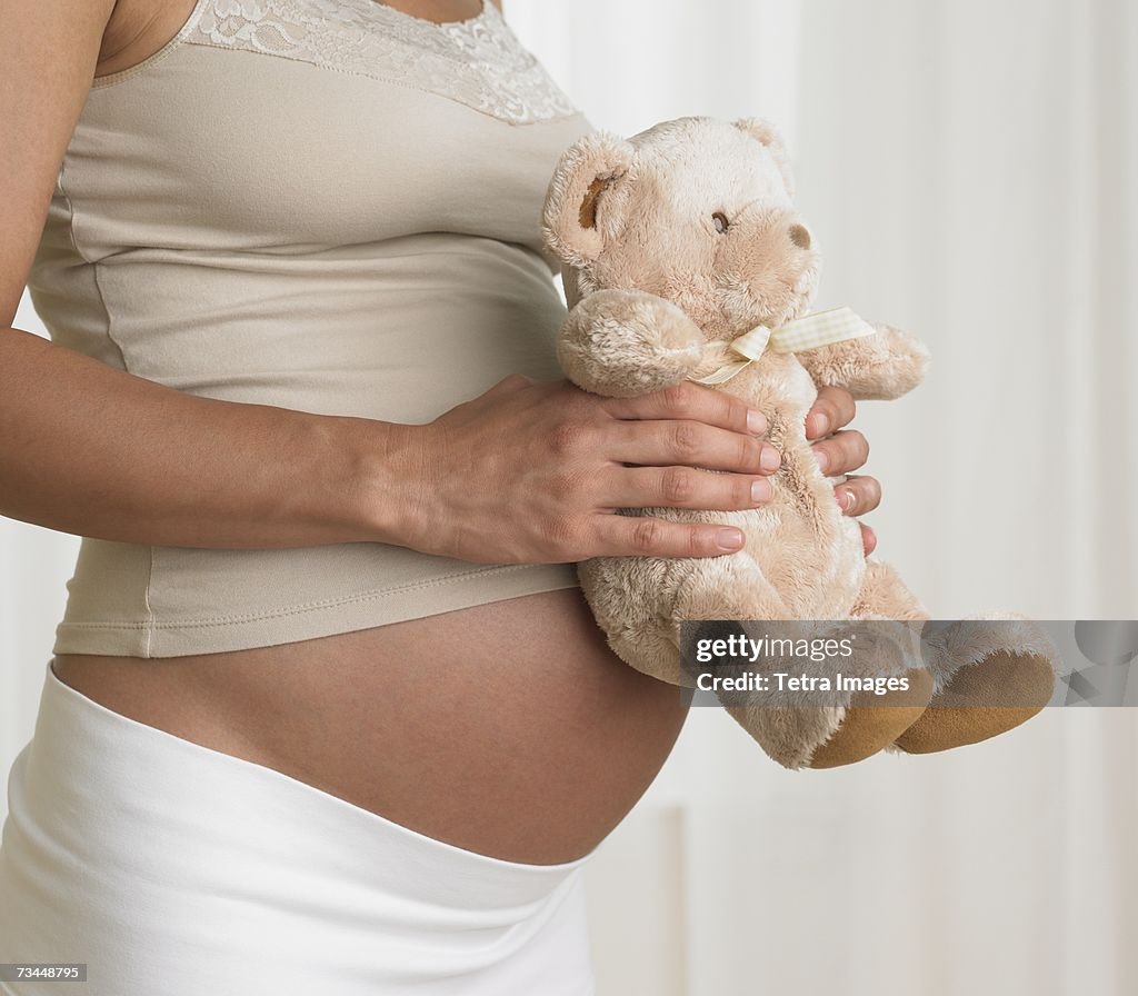 Pregnant woman holding teddy bear against stomach