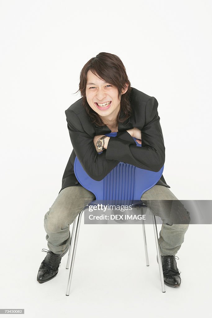 Portrait of a young man sitting on a chair and looking cheerful