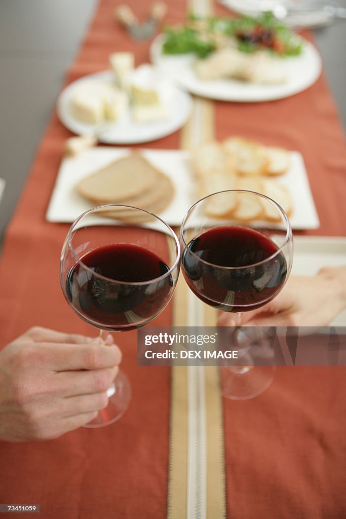 Close-up of two people toasting glasses of red wine