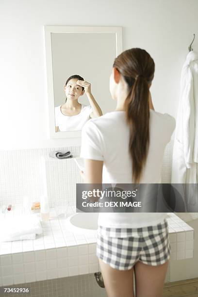 rear view of a young woman applying face powder on her forehead in front of a mirror - tap forehead stock pictures, royalty-free photos & images