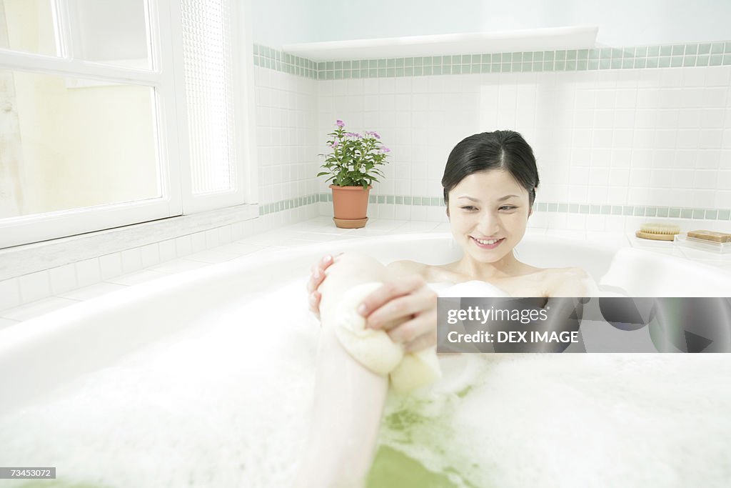 Young woman scrubbing her leg in a bathtub