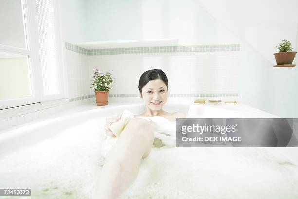 portrait of a young woman scrubbing her leg in a bathtub and smiling - japanese women bath stock pictures, royalty-free photos & images
