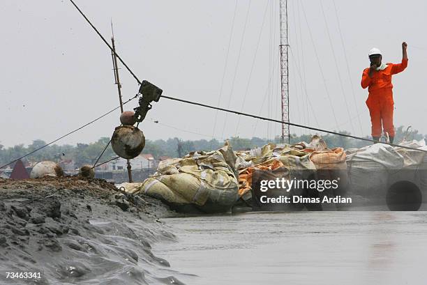 Indonesian workers give direction to crane operator as chained concrete balls are dropped in a crater to help stop a mudflow March 1, 2007 in...