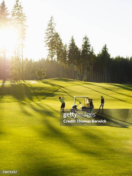 couple on golf course with golf cart, man swinging golf club - couple swinging stock pictures, royalty-free photos & images