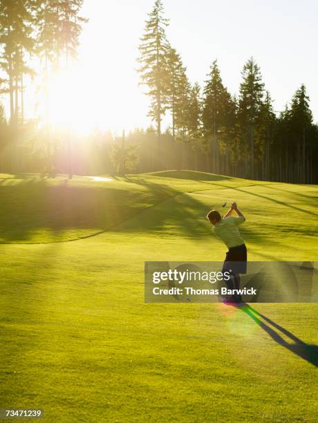 man swinging golf club on golf course, rear view - golf swing sunset stock pictures, royalty-free photos & images