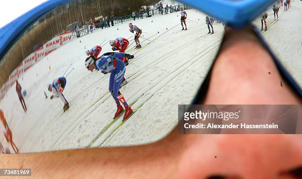 Swedish coach watches female athletes as they are reflected in his sunglasses during the mass start at the Women's 30km Classic Cross Country Event...