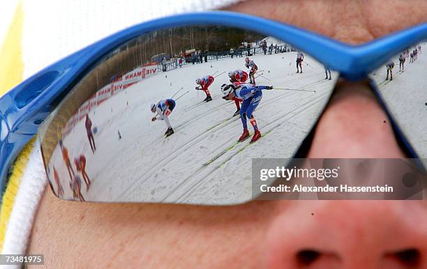 Swedish coach watches female athletes as they are reflected in his sunglasses during the mass start at the Women's 30km Classic Cross Country Event...