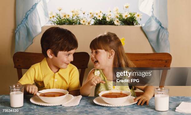 Boy and girl sharing a joke while eating tomato soup, circa 1970.