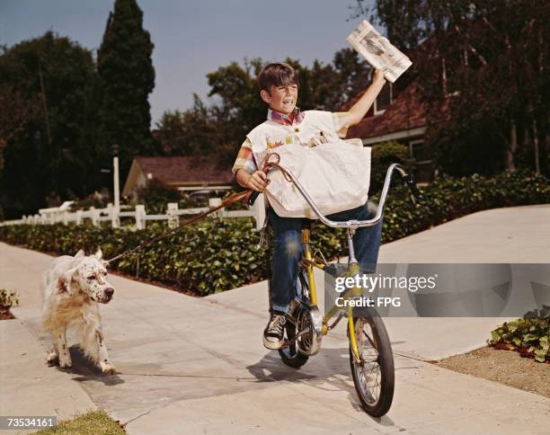 Boy riding his bike while delivering papers with his dog in tow, 1970s.