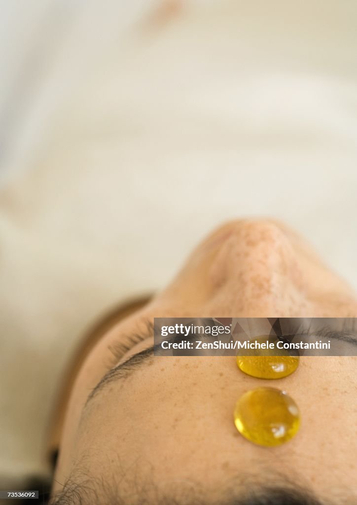 Woman reclining with two glass pebbles on forehead, close-up