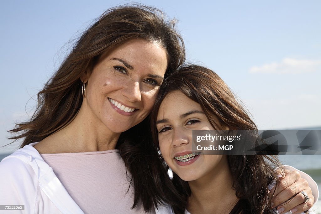 Mother and daughter (10-12) outdoors, smiling, portrait