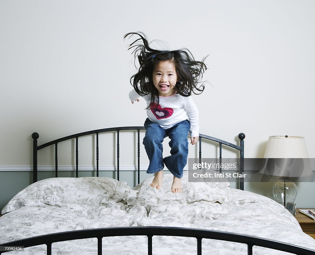 Girl (3-5) jumping on bed