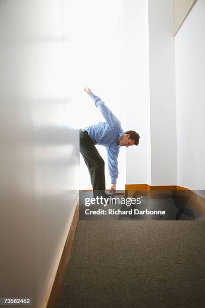 businessman bending to touch his toes in hallway - touching toes stock pictures, royalty-free photos & images