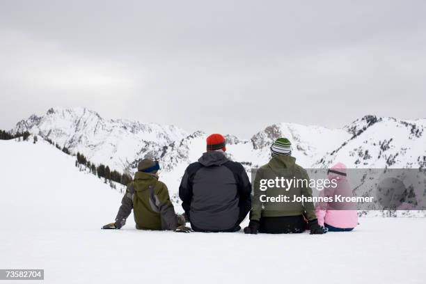 family, in skiwear, sitting side by side in mountain snow, looking at view, rear view - alta utah stock pictures, royalty-free photos & images