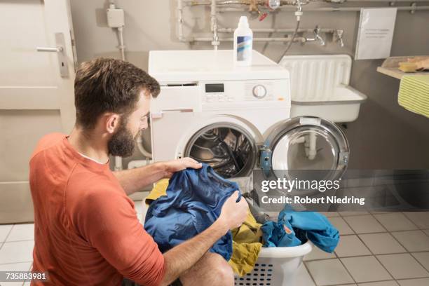 man sitting in front of washing machine with clothes in laundry basket - bavarian man in front of house stockfoto's en -beelden