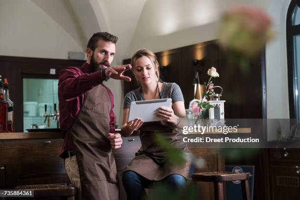 young restaurant owners discussing while sitting by bar counter - newtechnology stock pictures, royalty-free photos & images