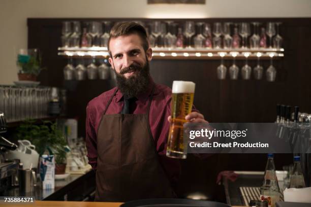portrait of young man offering glass of beer - bartenders stock-fotos und bilder