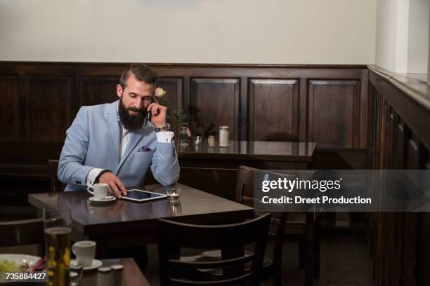 young man talking on phone while using digital tablet at restaurant - newtechnology fotografías e imágenes de stock