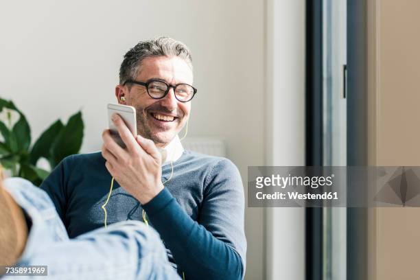 portrait of smiling businessman using smartphone and earphones - smartphone office stock-fotos und bilder
