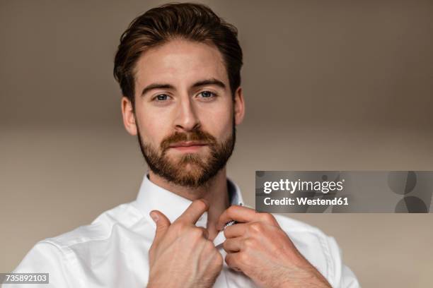 portrait of young businessman buttoning collar of his shirt - buttoning stock pictures, royalty-free photos & images