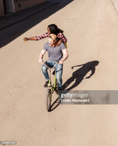 young man riding bicycle with his girlfriend standing on rack, taking selfies - velo humour stock-fotos und bilder