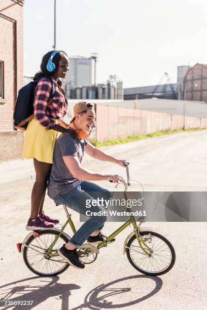 young couple riding bicycle with girl standing on rack - zusammenklappbar stock-fotos und bilder