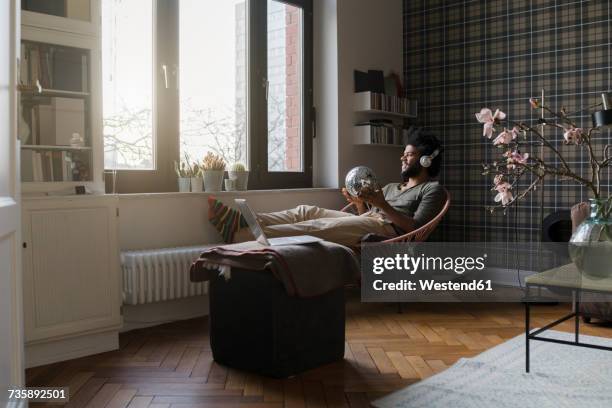 man sitting in living room in armchair holding mirror ball listening to music - music home stock-fotos und bilder