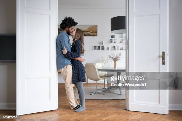 kissing couple at home standing in door frame in living room - couple kissing stock-fotos und bilder