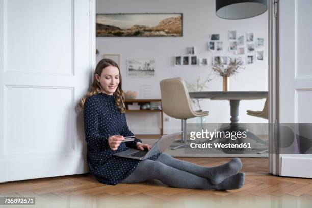 smiling woman at home sitting on floor with laptop in door frame holding credit card - blank frame stockfoto's en -beelden