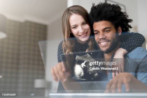 Smiling couple looking at ultra sound picture of baby on futuristic screen