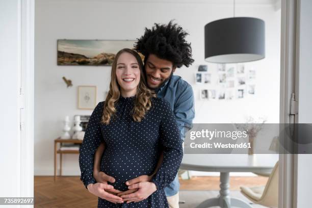 smiling pregnant couple in living room - couple mixed race stock pictures, royalty-free photos & images