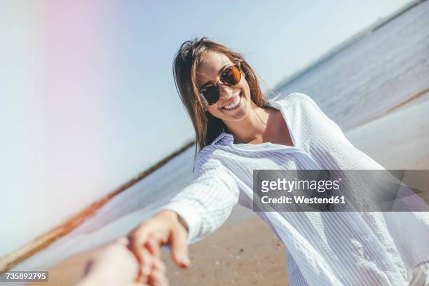 portrait of smiling young woman with sunglasses holding hand on the beach - bluse stock-fotos und bilder