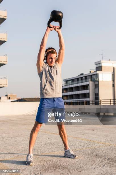 young man exercising with kettle bell on a rooftop - kettle bells fotografías e imágenes de stock