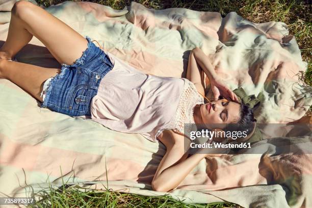 young woman lying on blanket listening music with headphones - shorts foto e immagini stock