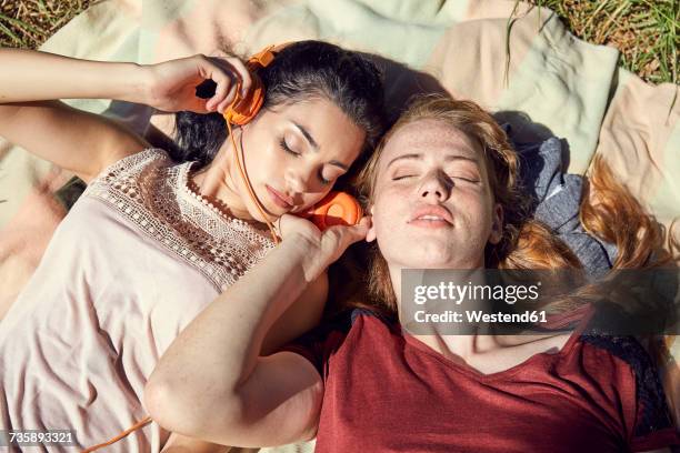 portrait of two young women lying side by side on blanket listening music with headphones - sharing headphones stock pictures, royalty-free photos & images