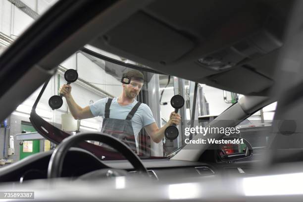 car mechanic in a workshop changing car window - windscreen stockfoto's en -beelden