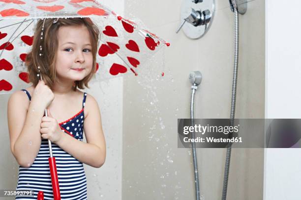 portrait of smiling little girl taking shower with umbrella - wc hart stockfoto's en -beelden