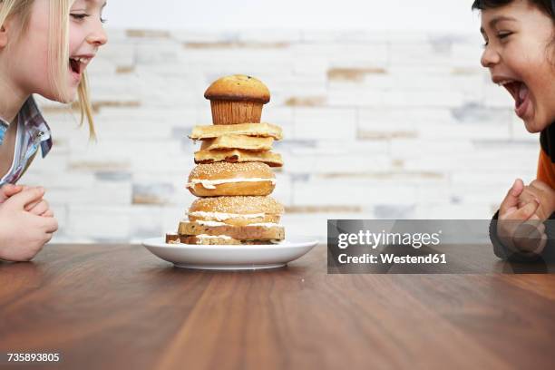 two hungry children with stack of baked goods - brot mund stock-fotos und bilder