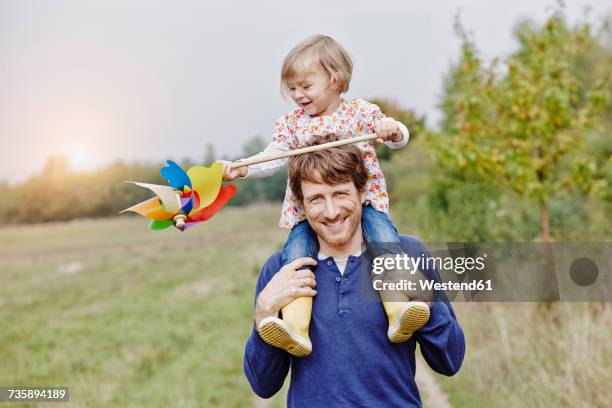 father carrying daughter with pinwheel on shoulders - windrad stock-fotos und bilder
